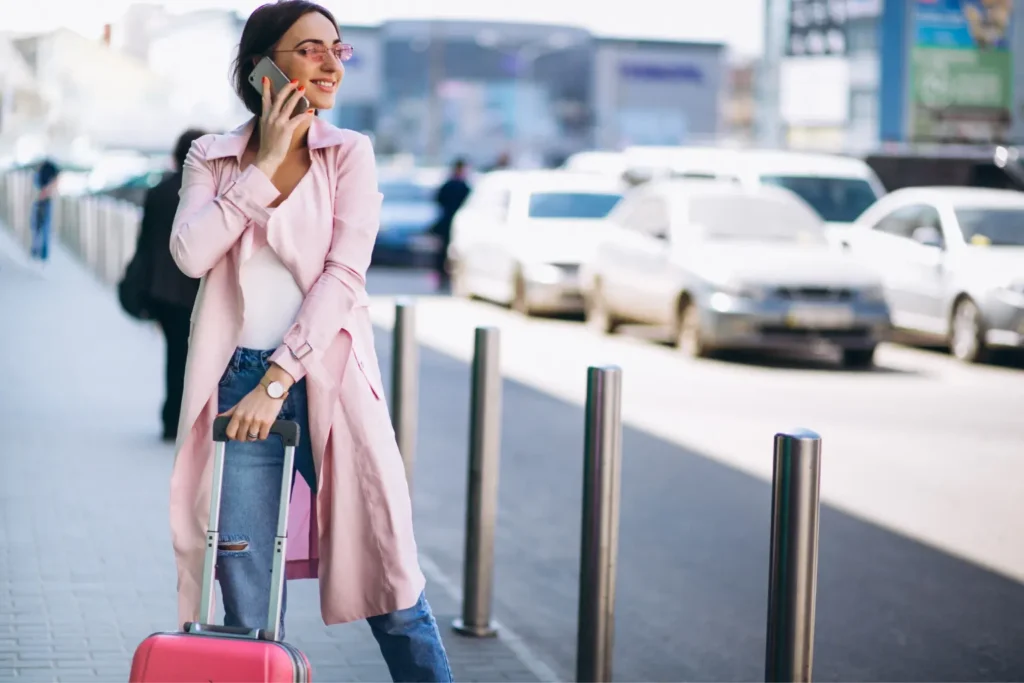 Liss Airport Transfers – traveler with luggage using her phone outside the airport terminal