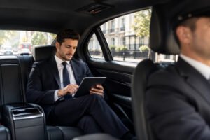 Business traveller using a tablet in the back seat while a professional chauffeur drives